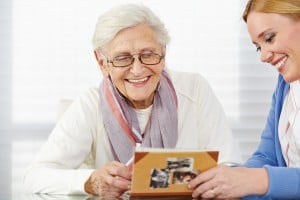Lächelnde Seniorin schaut Fotos im Fotoalbum an mit ihrer Tochter
